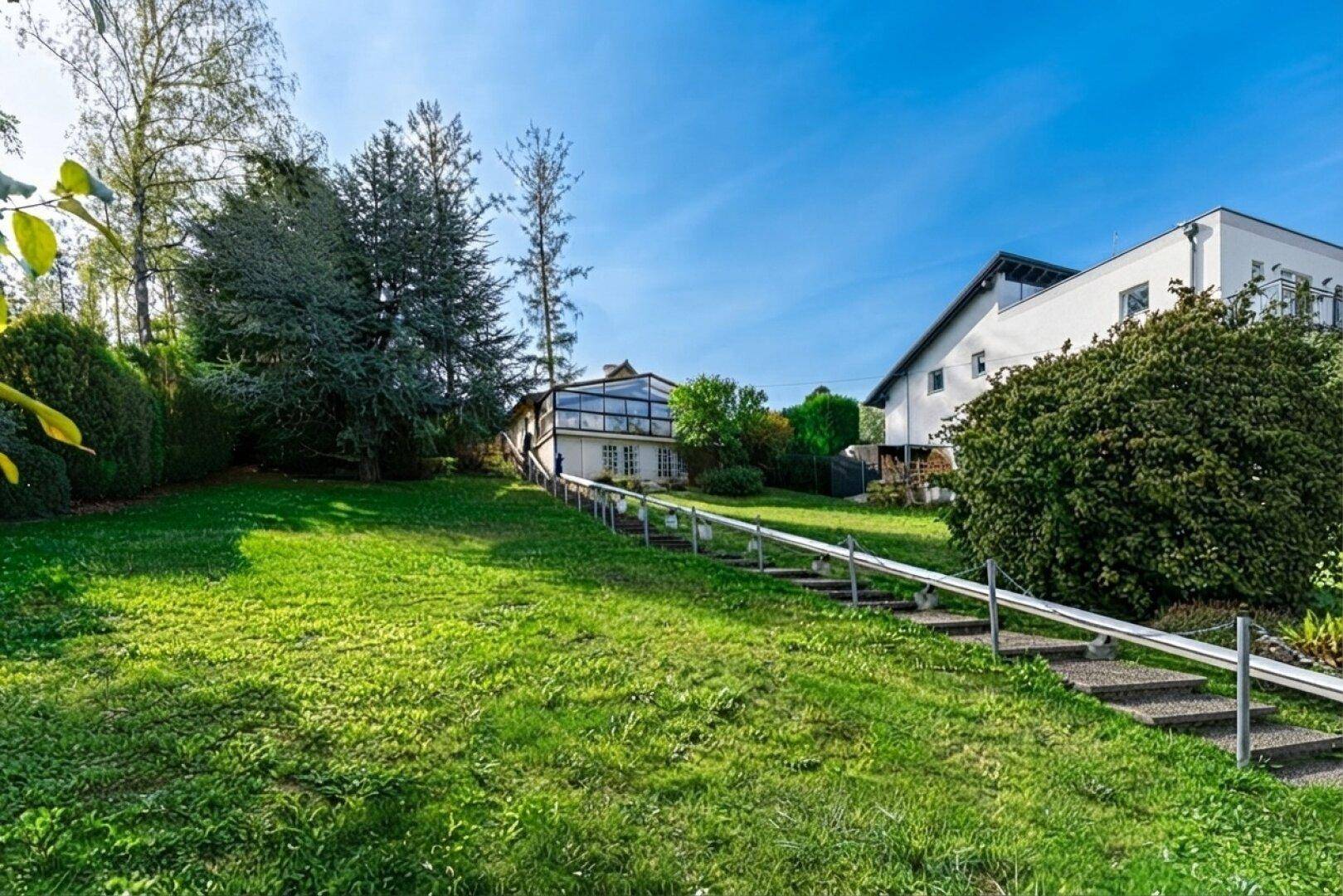Haus auf einem Hanggrundstück mit großem Garten, Treppe und umliegender Natur.