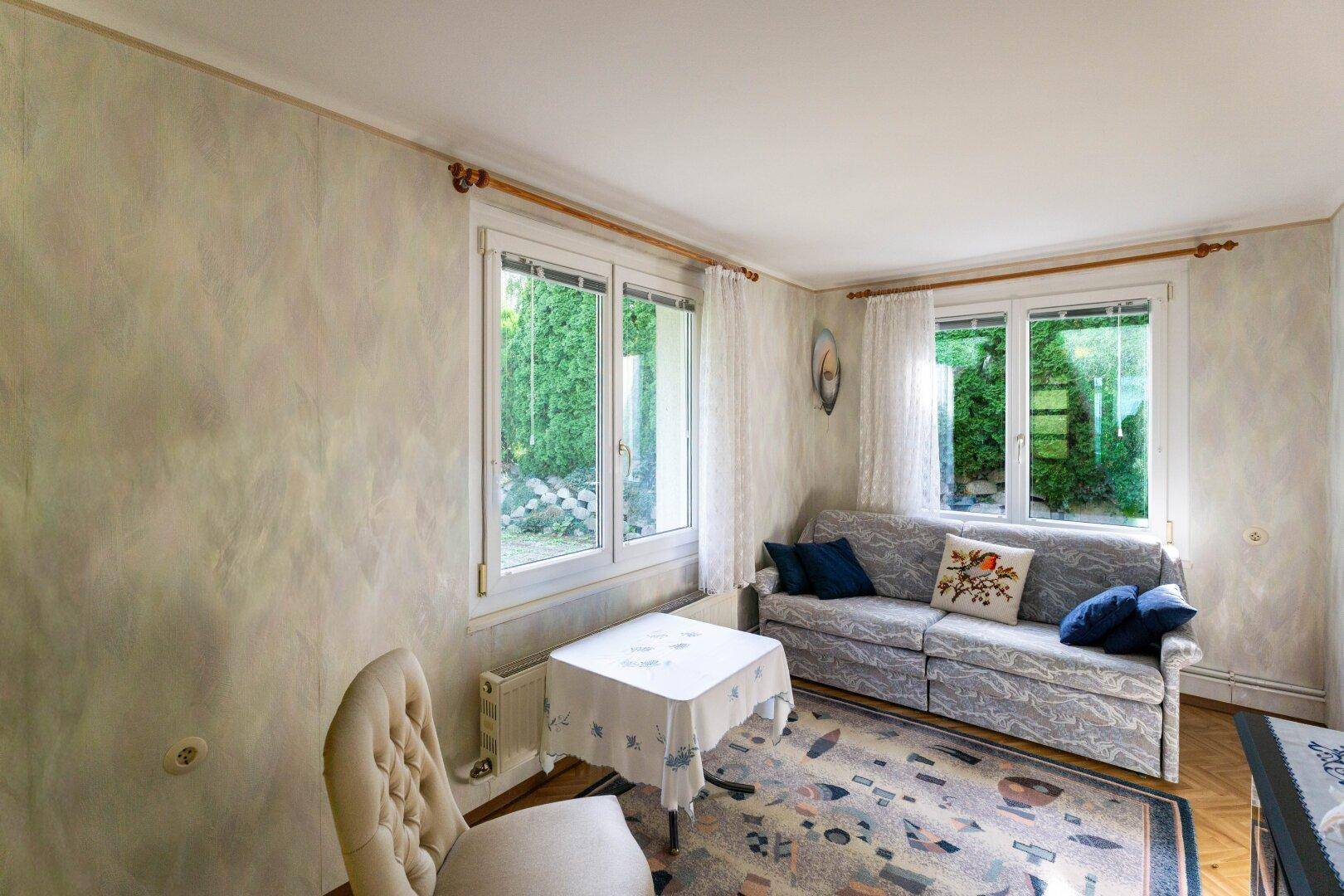 Gemütliches Wohnzimmer mit Sofa, Teppich und Blick in den grünen Garten.