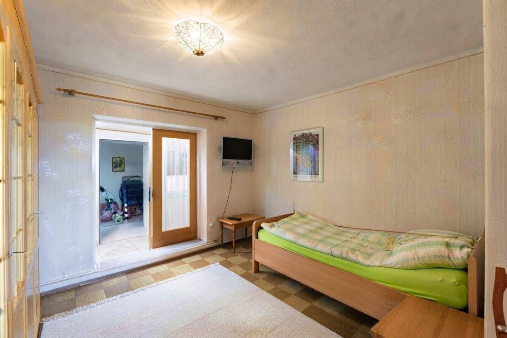 Schlafzimmer mit Einzelbett, Schrank und Zugang zu einem weiteren Raum.
