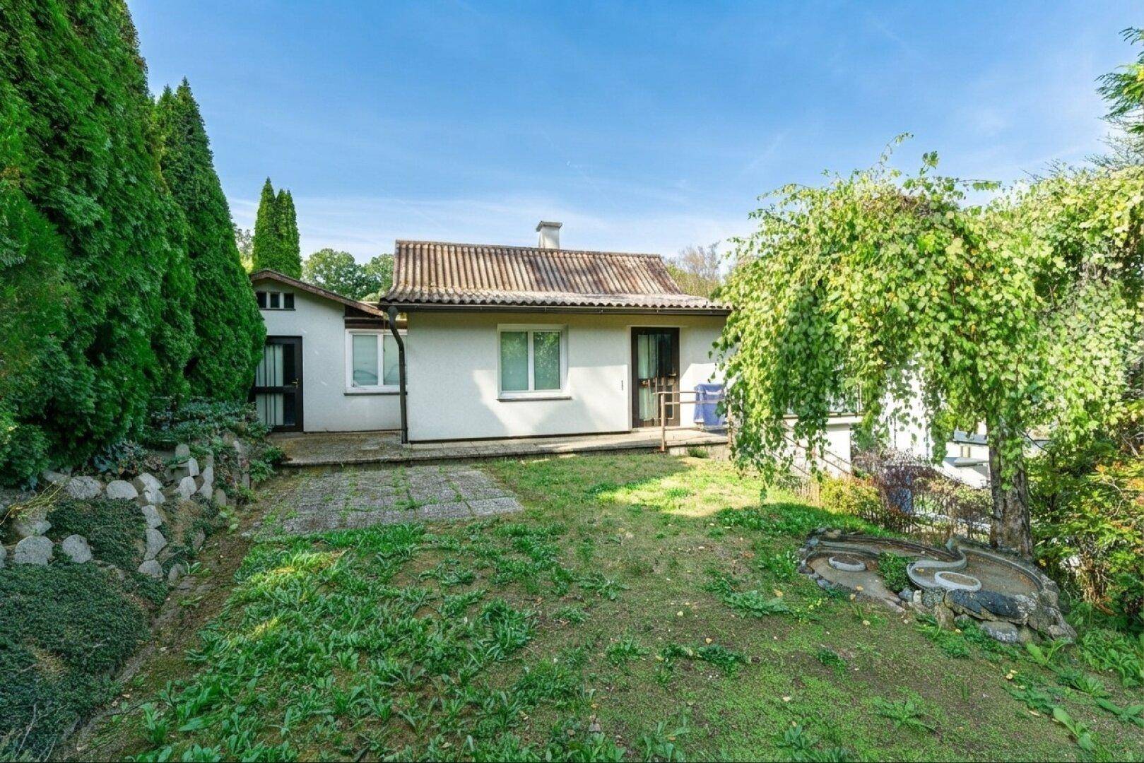 Rückseite des Hauses mit kleiner Terrasse, Garten und üppiger Bepflanzung.
