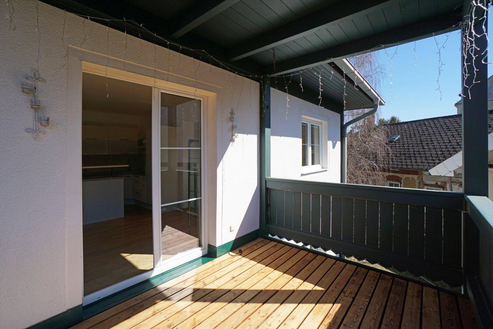 Heller Balkon mit Holzdielenboden und dunklem Holzgeländer, bietet Zugang zum Innenbereich.