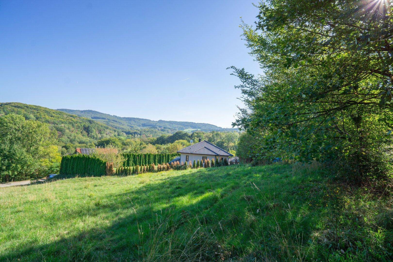 Idyllische Landschaft mit einem Haus auf einem Hügel, umgeben von Wald und weitem Blick.