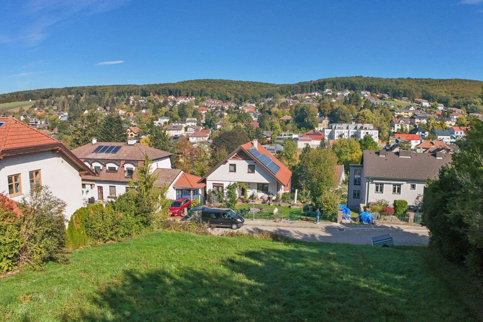 Panoramablick von der Wiese auf die Nachbarschaft mit verschiedenen Häusern und bewaldeten Hügeln im Hintergrund.