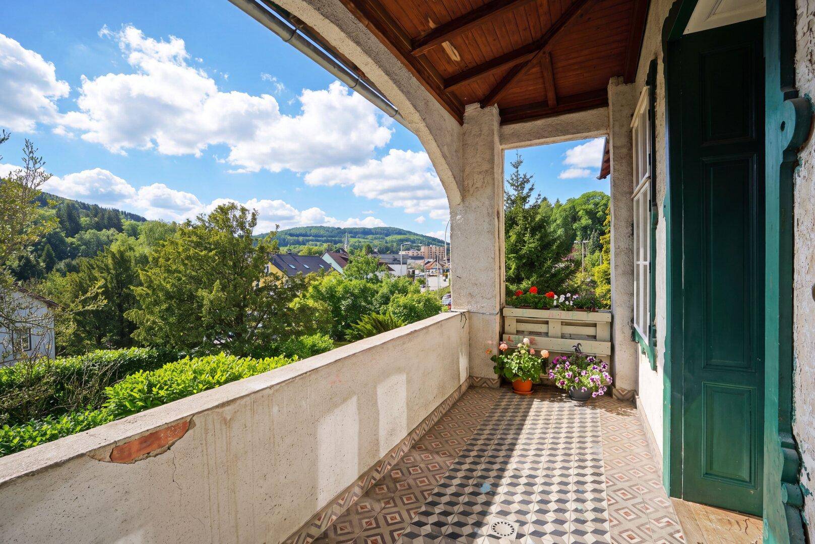 Überdachter Balkon mit Fliesenboden und weitem Blick über die grüne Landschaft und Häuser.