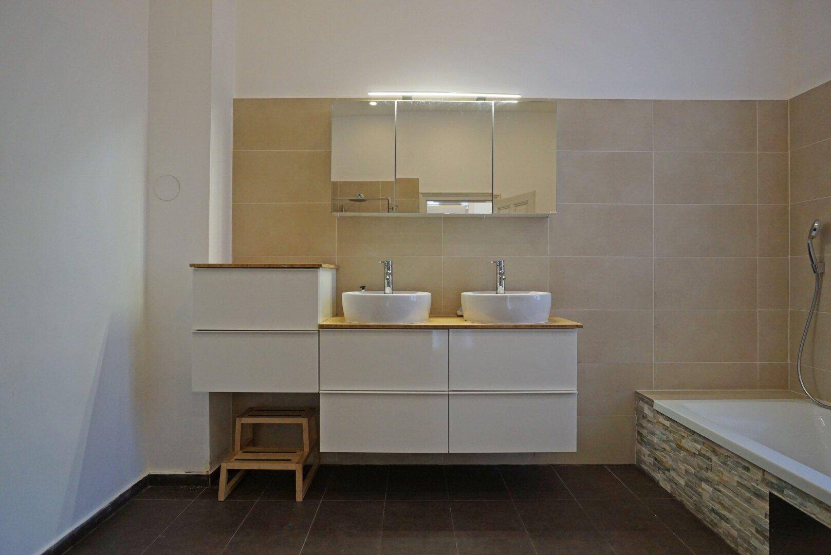 Modernes Badezimmer mit Doppelwaschbecken, Badewanne und beigefarbenen Fliesen an den Wänden.