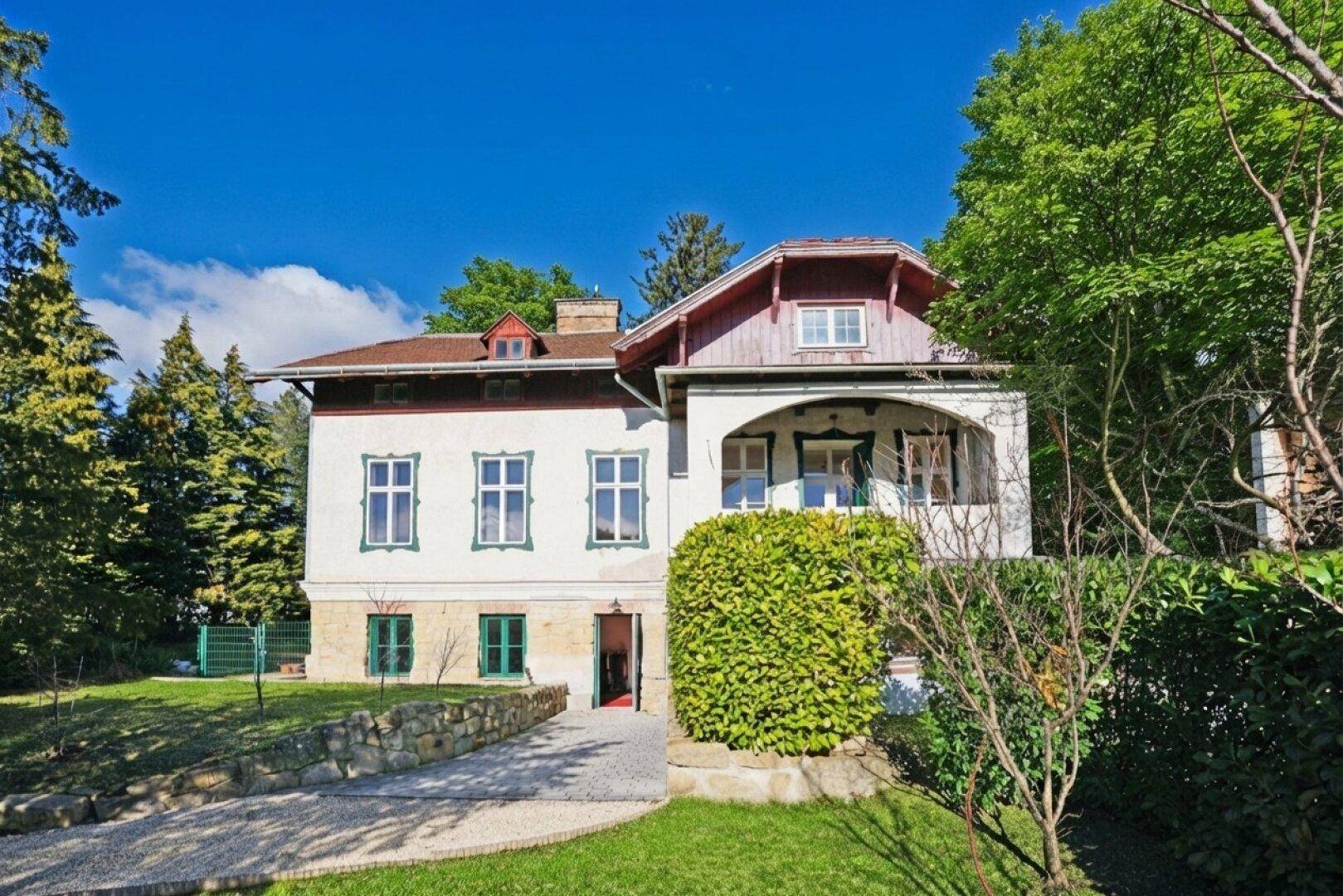 Historisches Gebäude mit weißer Fassade, grünen Fensterläden und umgebendem Garten.