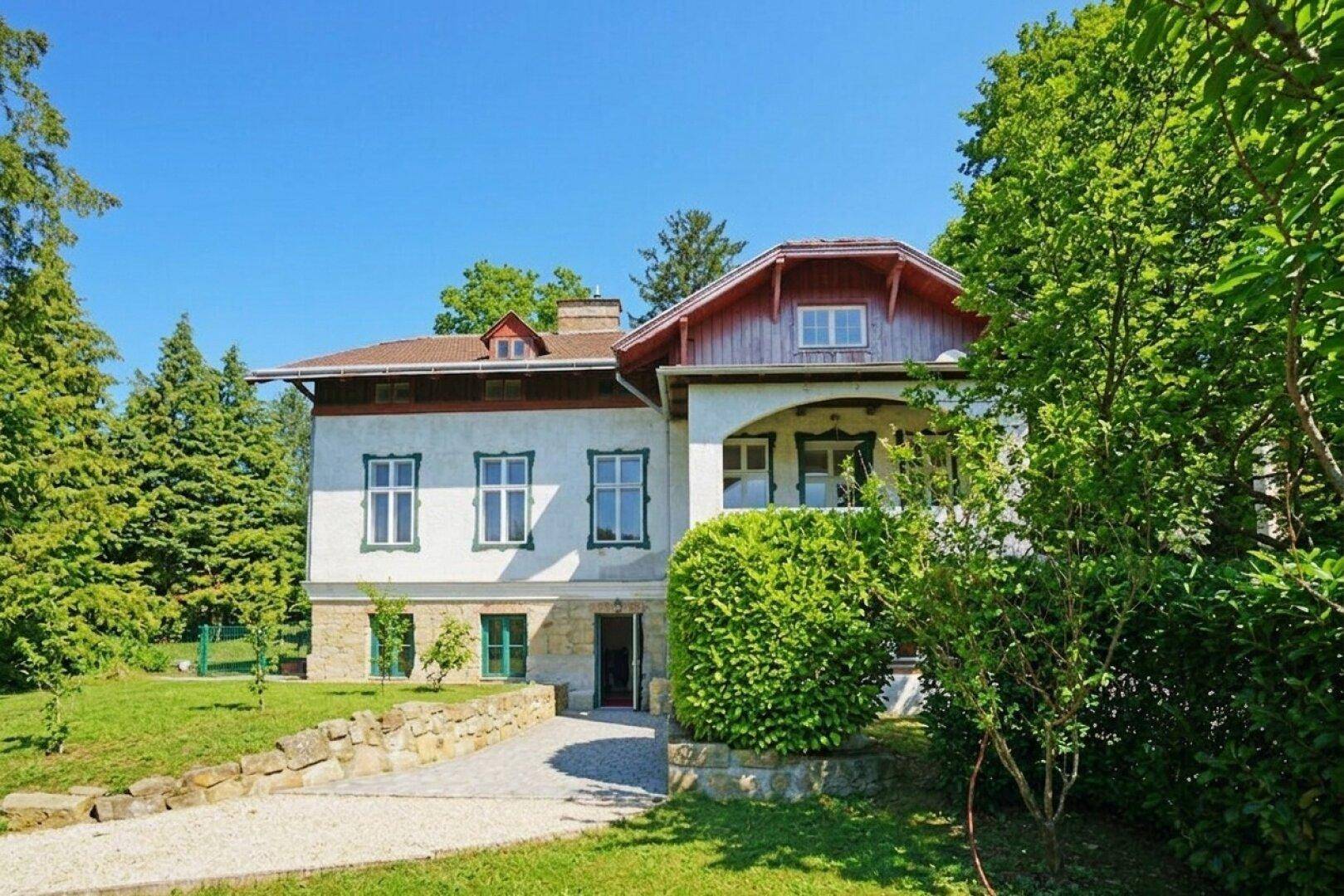 Historisches Gebäude mit gepflegtem Garten, umgeben von Bäumen und grüner Landschaft.