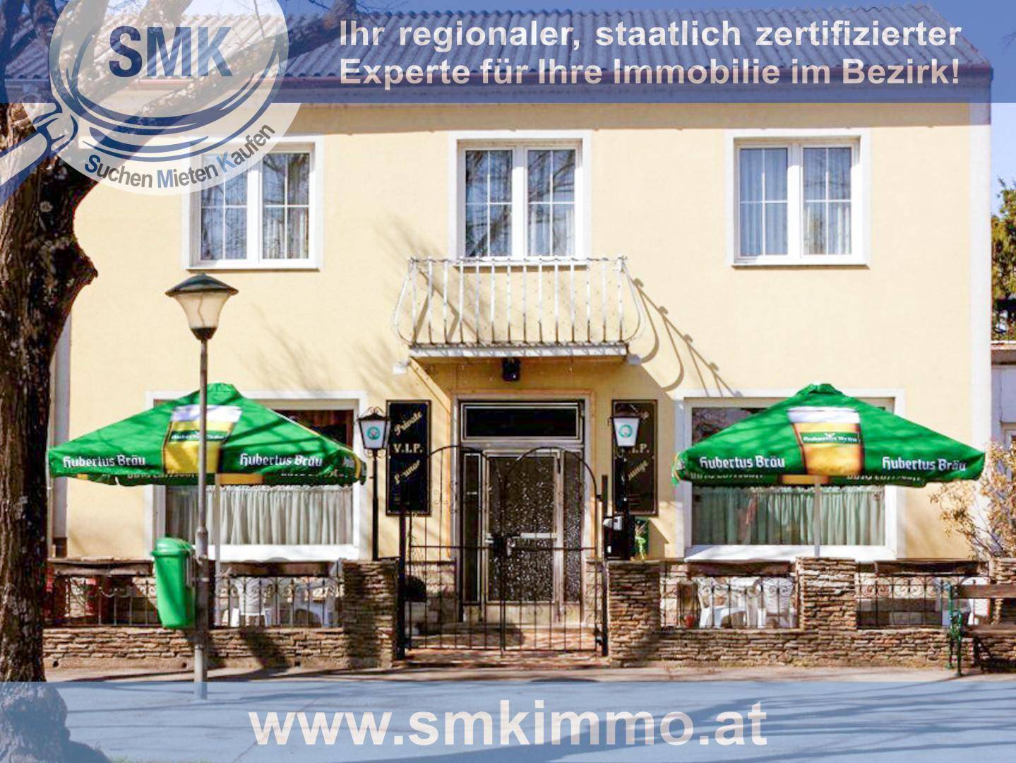 Nahaufnahme der Gebäudefassade mit Eingangsbereich, Fenstern und Außensitzplätzen.