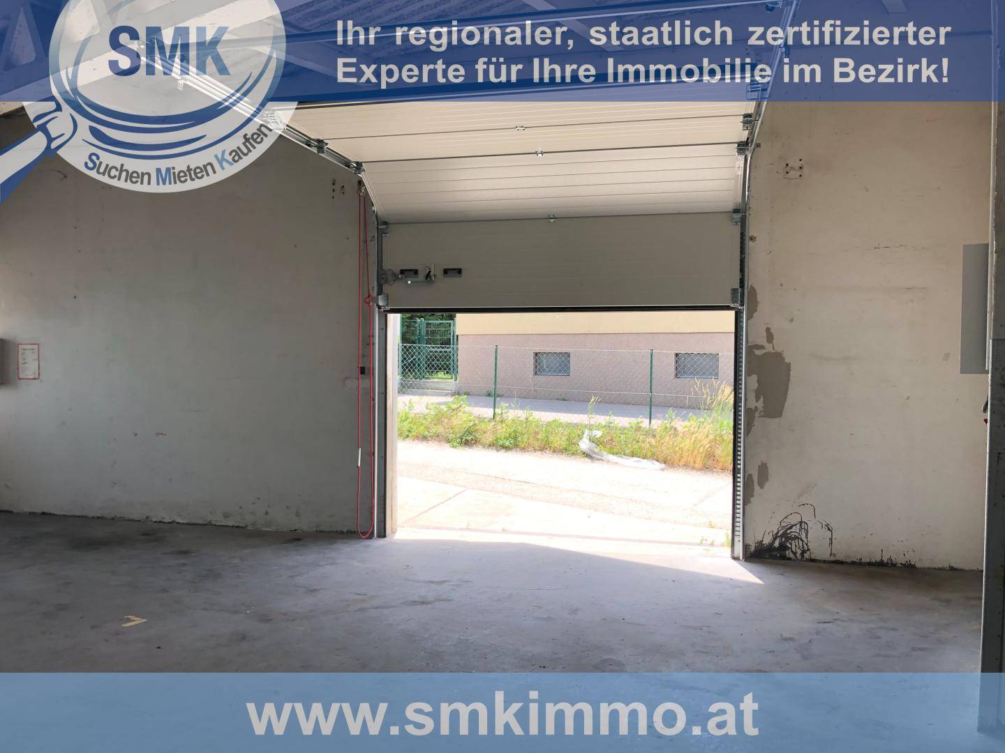 Innenansicht einer leeren Lagerhalle mit offenem Rolltor, das den Blick nach draußen freigibt.