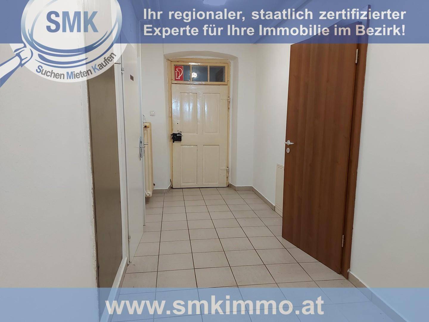 Langer Flur mit Fliesenboden und einer alten Holztür am Ende, der zu weiteren Räumen führt.
