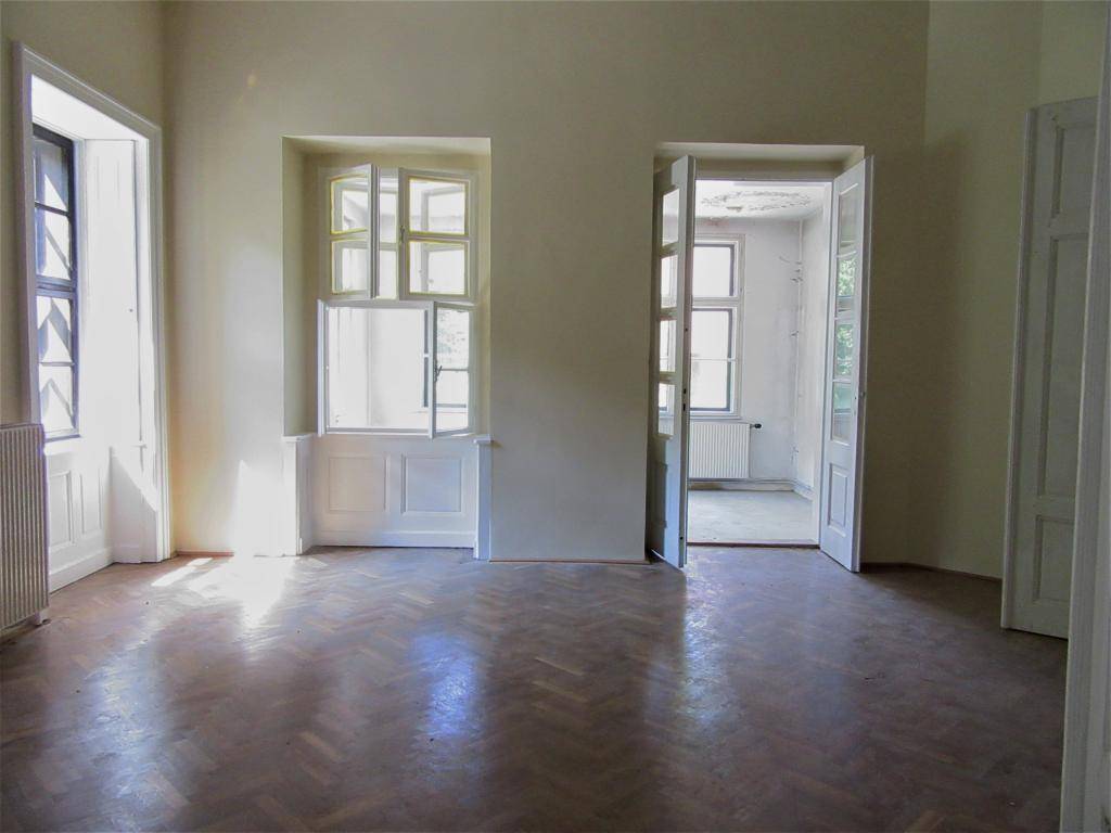 Heller, leerer Raum mit Fischgrätparkettboden und hohen Fenstern, bereit zur Renovierung.