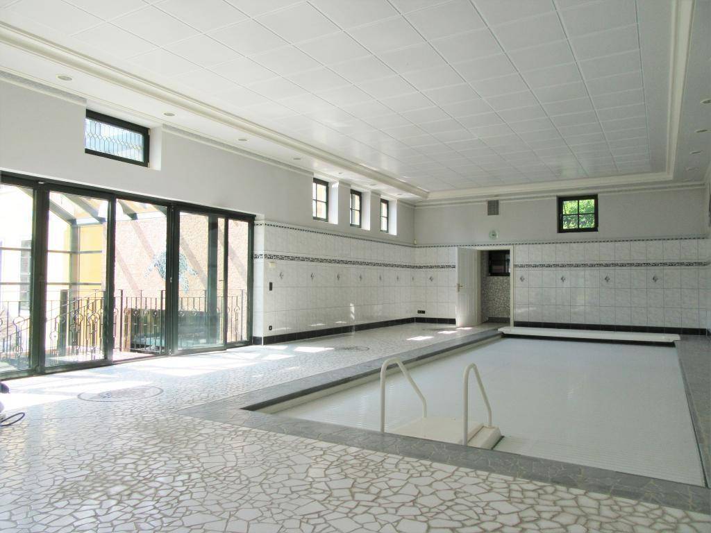 Großer Innenpoolbereich mit Mosaikboden und Glasfront, die viel Licht hereinlässt.