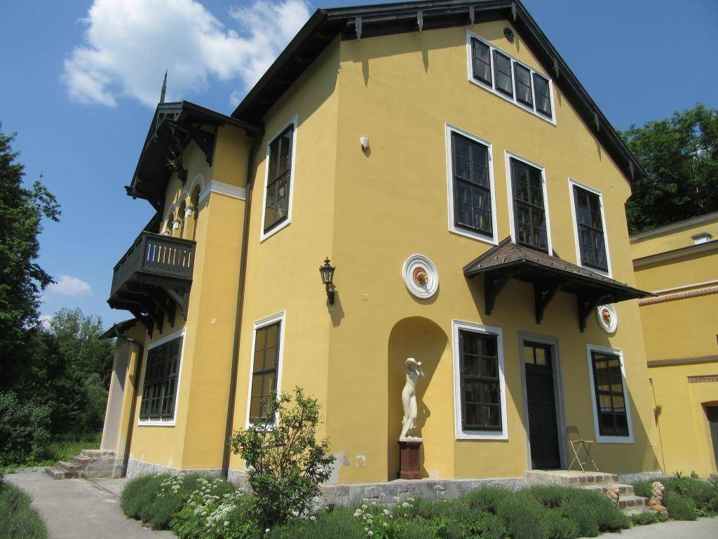 Prächtiges gelbes Gebäude mit klassischer Architektur, kleinem Balkon und einer Statue im Vorgarten.