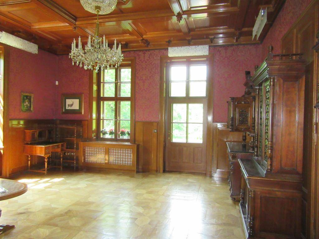 Prunkvolles Wohnzimmer mit Parkettboden, Holzdecke und einem opulenten Kronleuchter, viel Licht.