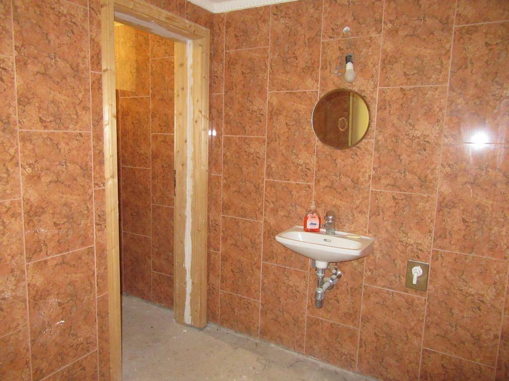 Badezimmer mit braunen Fliesen, einem Waschbecken und einem runden Spiegel, renovierungsbedürftig.