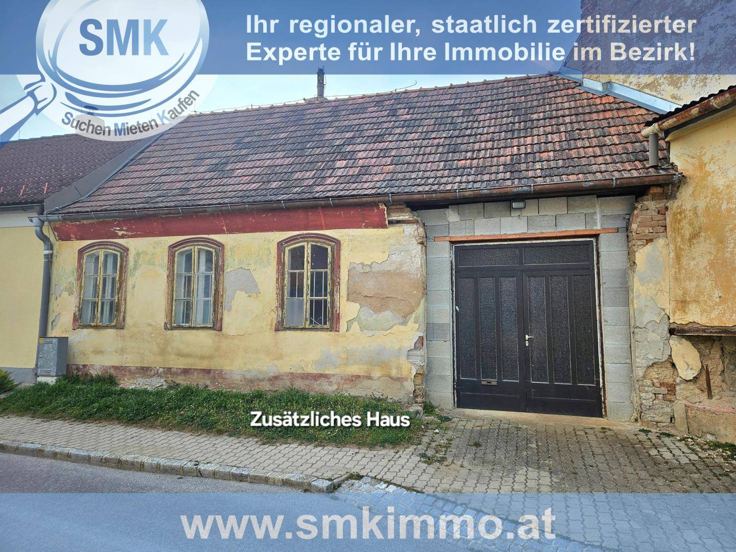 Altes Gebäude mit verputzter Fassade, Holztüren und einem großen Garagentor.