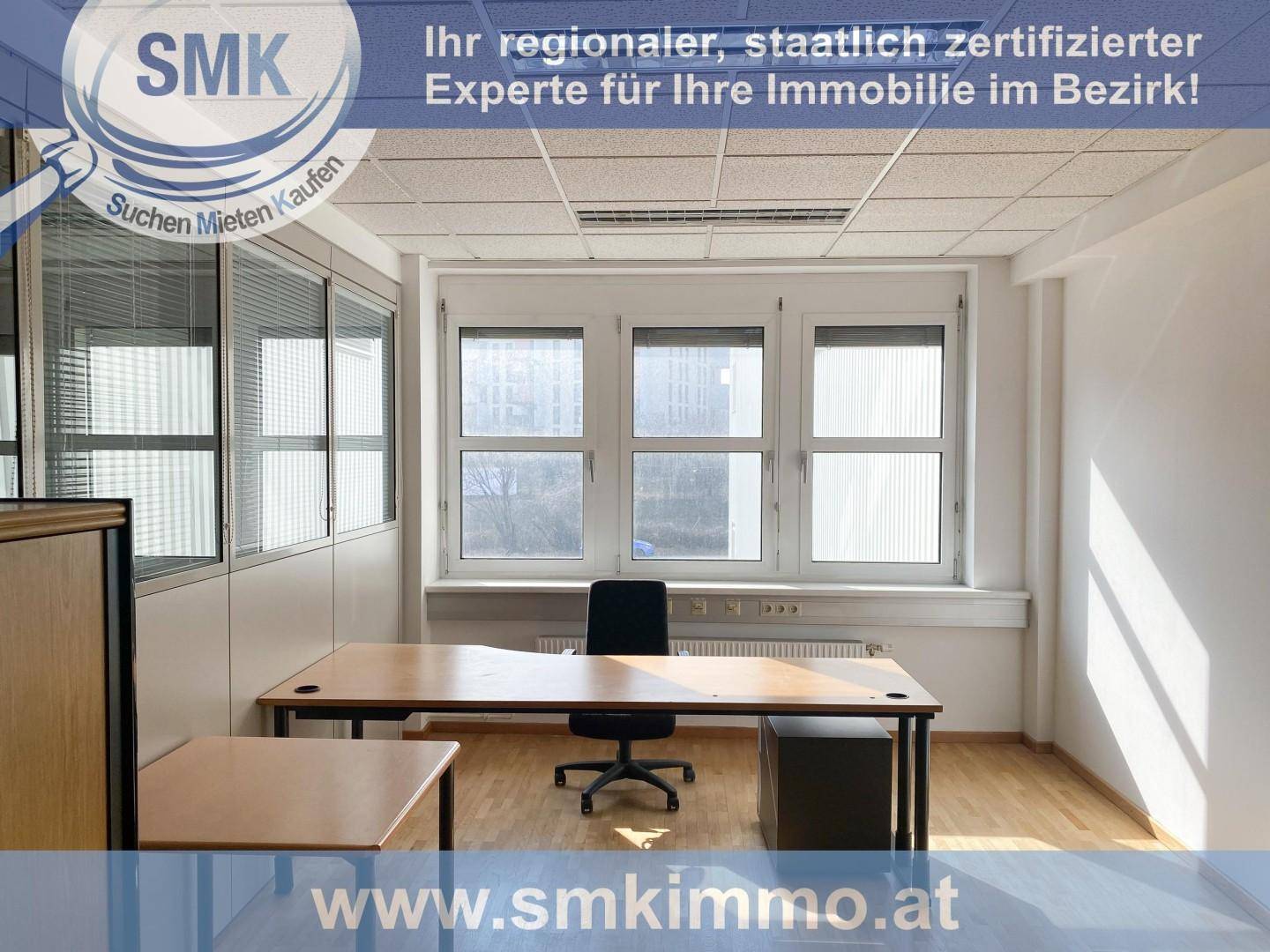 Möbliertes Büro mit Schreibtisch, Bürostuhl und großen Fenstern, die viel Tageslicht hereinlassen.