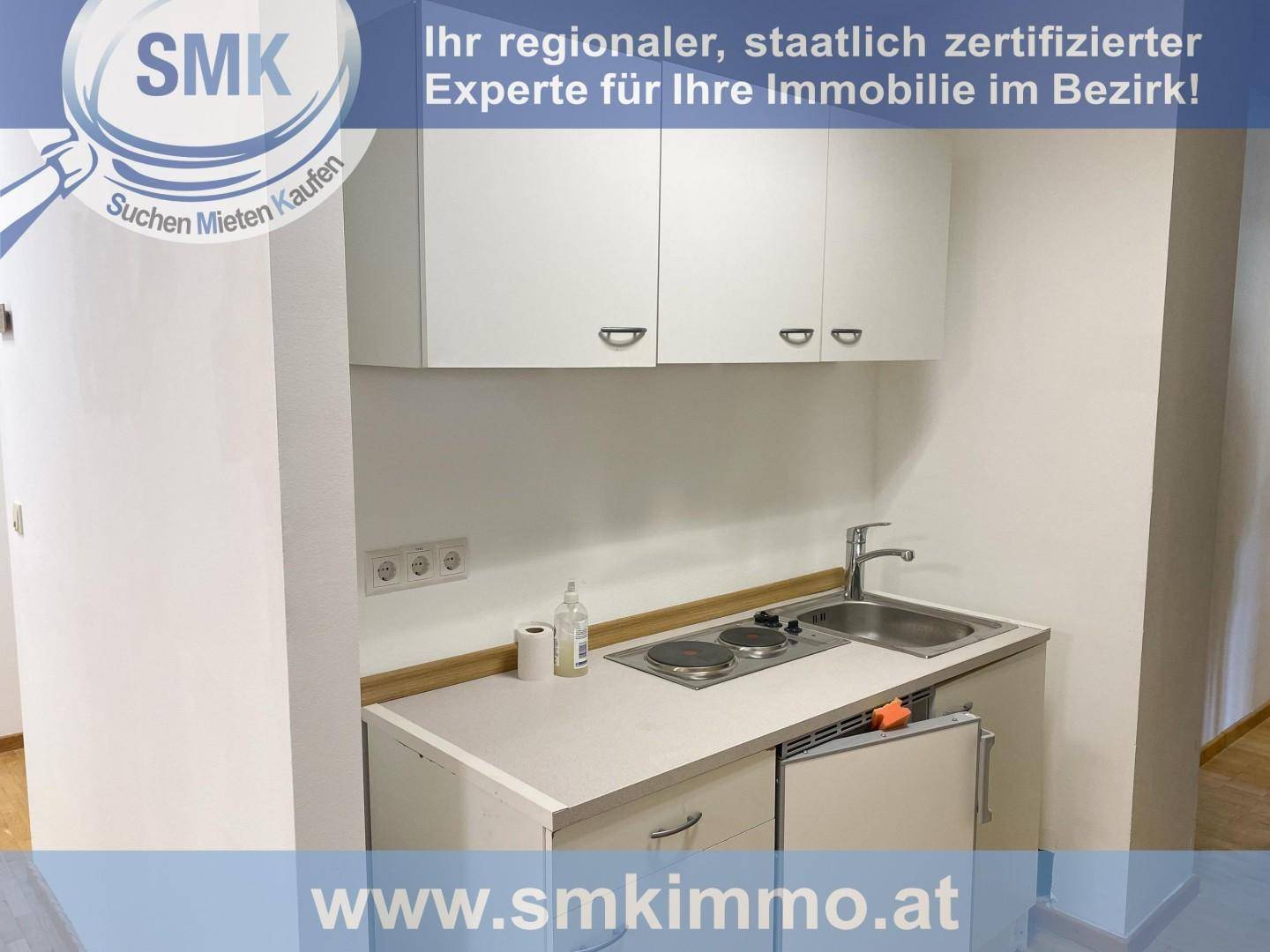 Kompakte Küchenzeile mit weißen Schränken, Spüle, Kochplatten und kleinem Kühlschrank, ideal für Büros.
