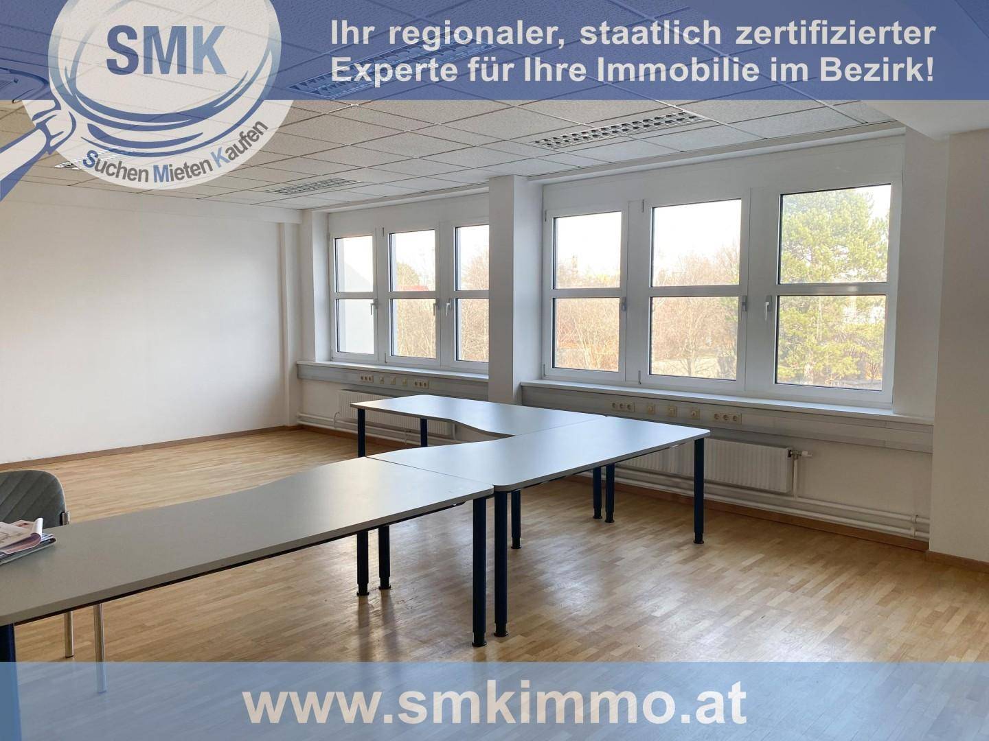 Heller Büroraum mit mehreren Tischen, großen Fenstern und Holzfußboden, ideal für Besprechungen oder Arbeitsplätze.