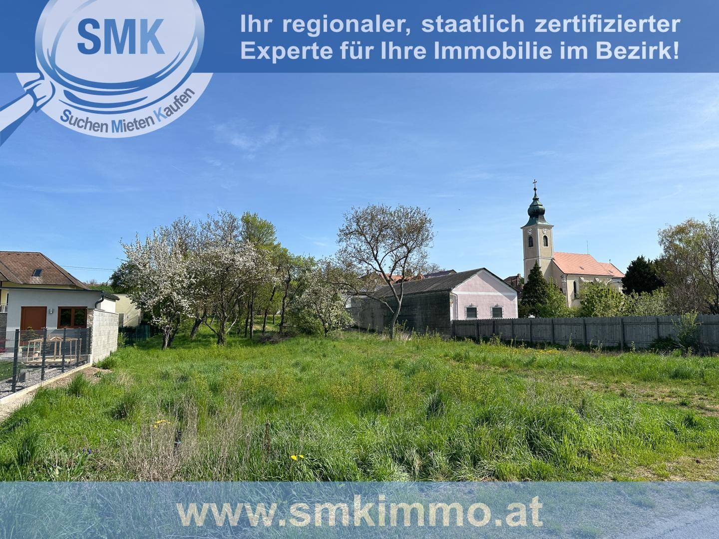 Offenes Grundstück mit Gras und Bäumen, im Hintergrund ist eine Kirche mit Turm sichtbar.