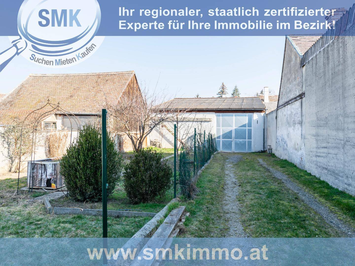 Gartenbereich mit unbefestigtem Weg und Blick auf ein Nebengebäude mit großen Fenstern.