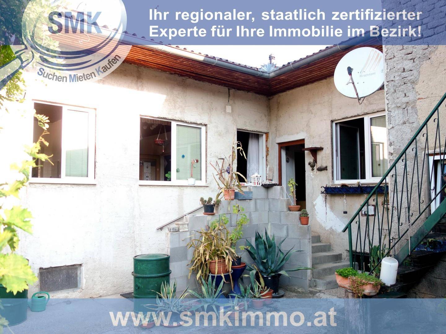Ecke eines Hauses mit Außentreppe, vielen Topfpflanzen und einer rauen Fassade.