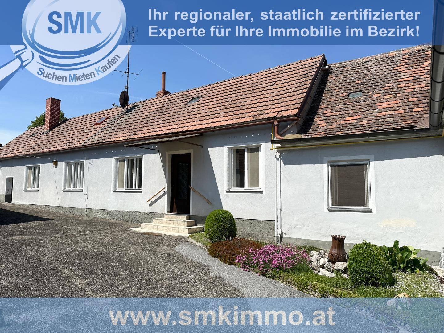 Ländliches Haus mit weißer Fassade, Ziegeldach und einem kleinen Vorgartenbereich.