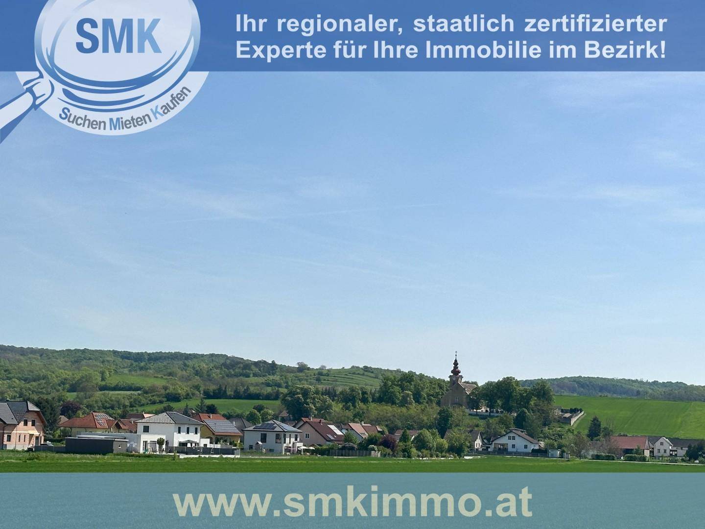 Panoramablick auf ein idyllisches Dorf mit Kirche, umgeben von grünen Hügeln und Feldern.