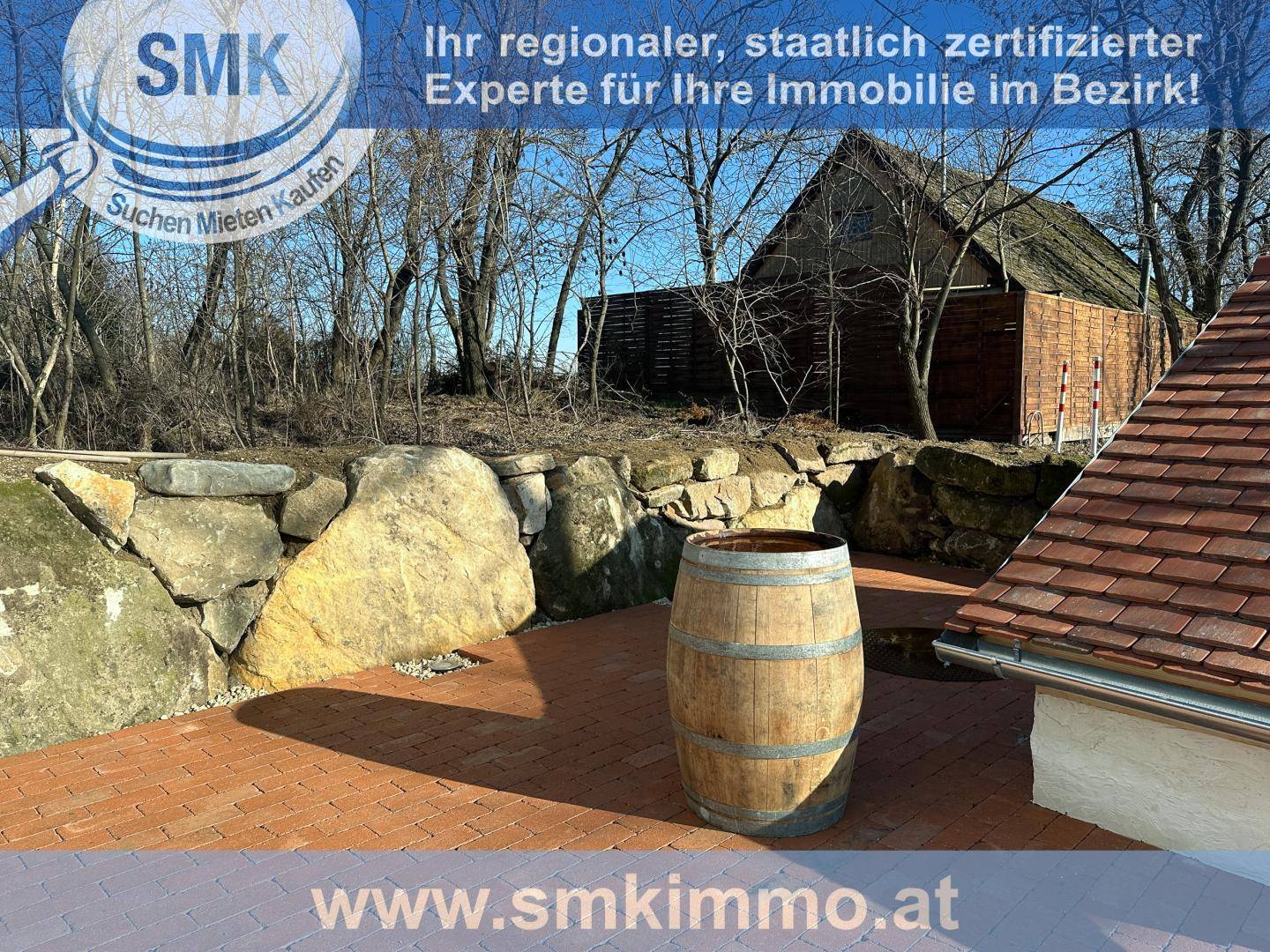 Gepflasterte Terrasse mit Steinmauer und einem dekorativen Holzfass im Freien.