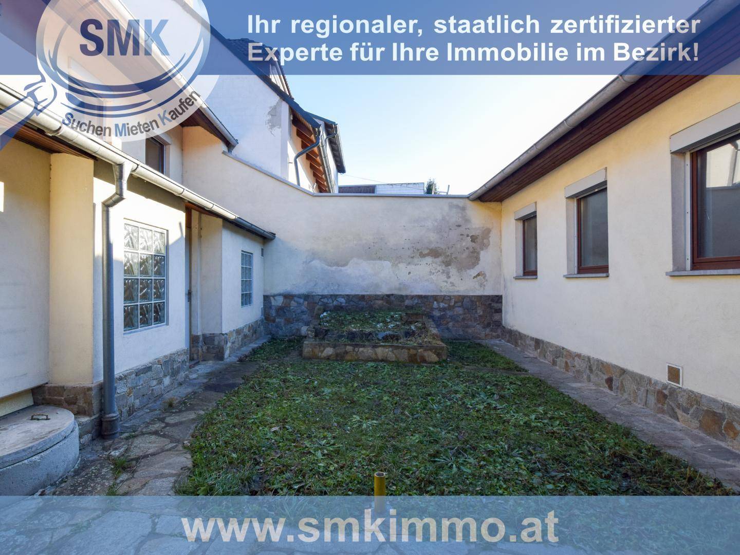 Kleiner Hinterhofgarten mit Rasenfläche, Steinplatten und umgebenden Mauern.