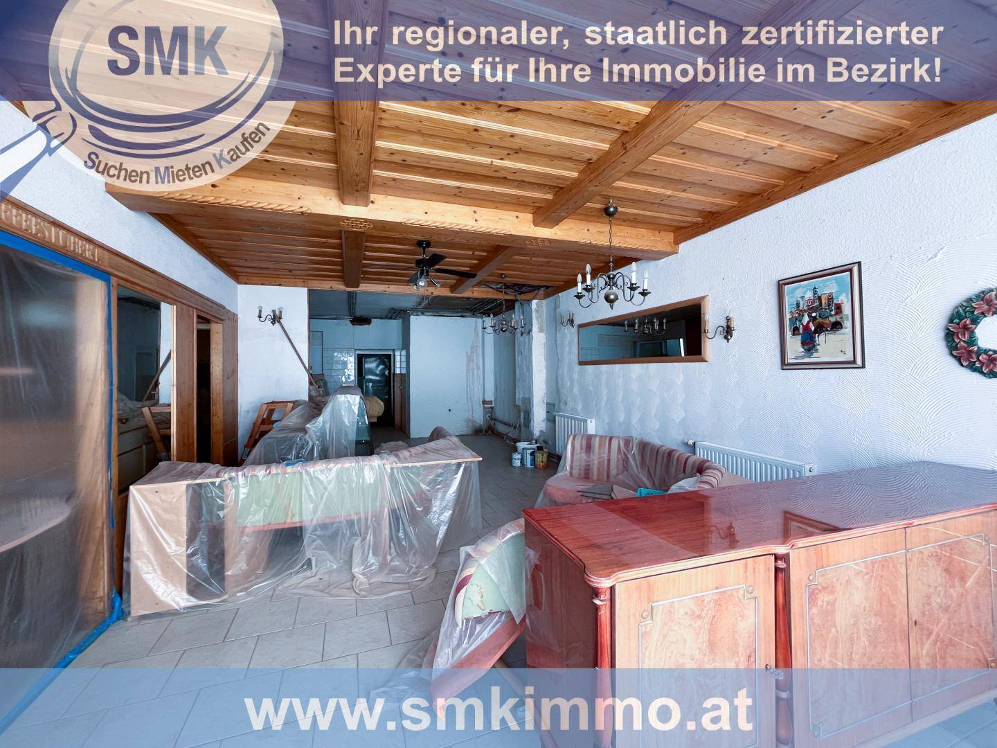 Renovierungsbedürftiger Raum mit sichtbaren Holzdeckenbalken und abgedeckten Möbeln.