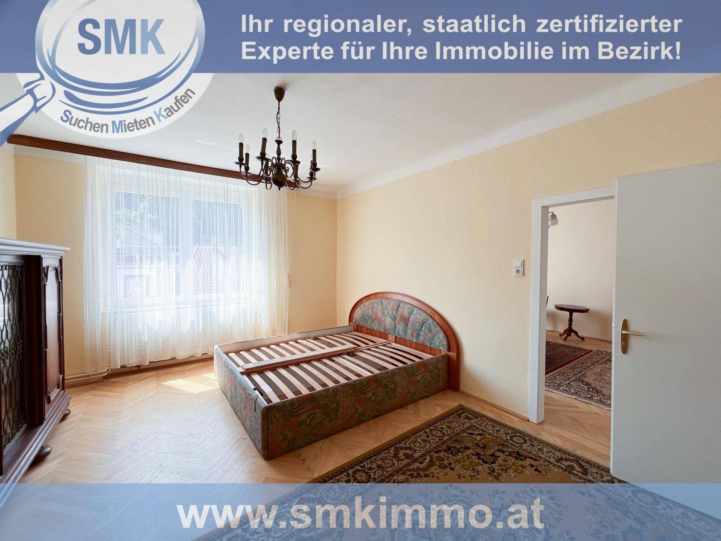 Helles Schlafzimmer mit Parkettboden, großem Fenster und klassischem Bettrahmen.