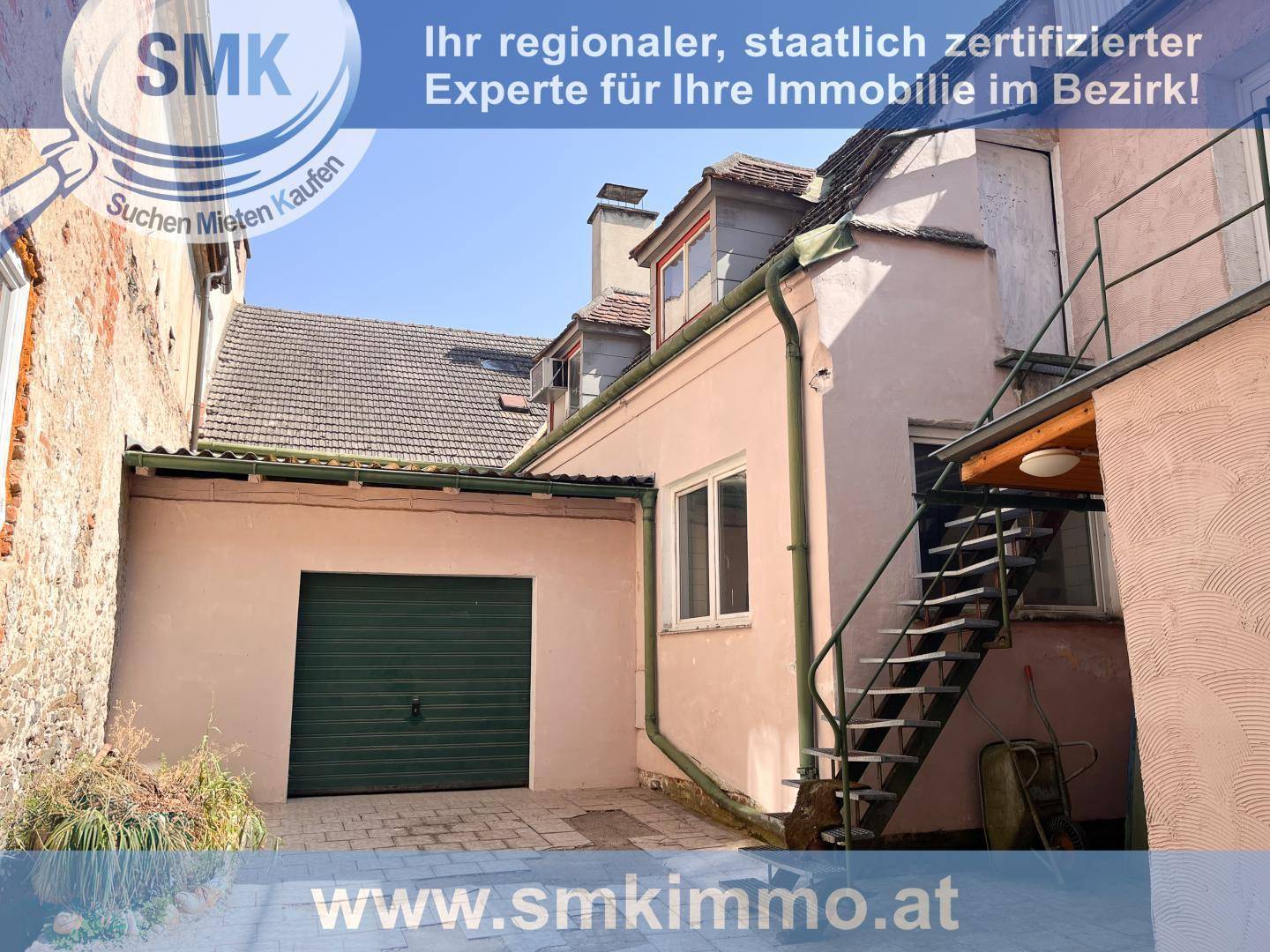 Rückansicht eines Gebäudes mit Außentreppe und Garagentor in einem Hinterhof.