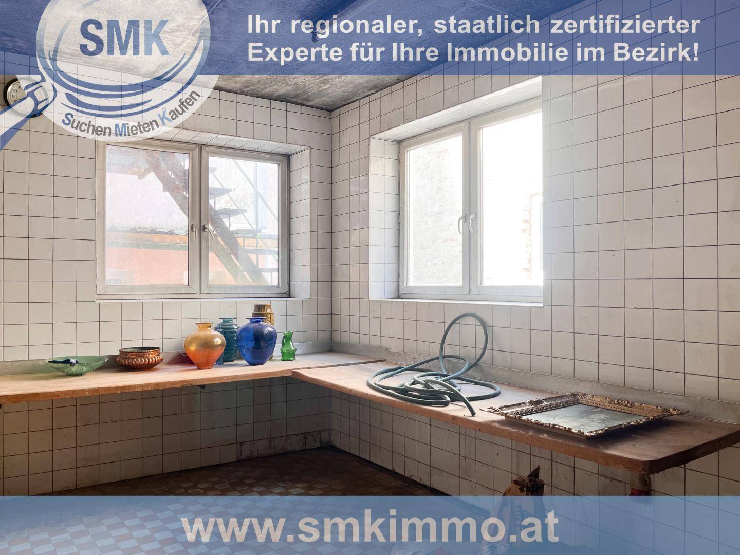 Funktionaler Hauswirtschaftsraum mit gefliesten Wänden, Arbeitsflächen und zwei Fenstern.