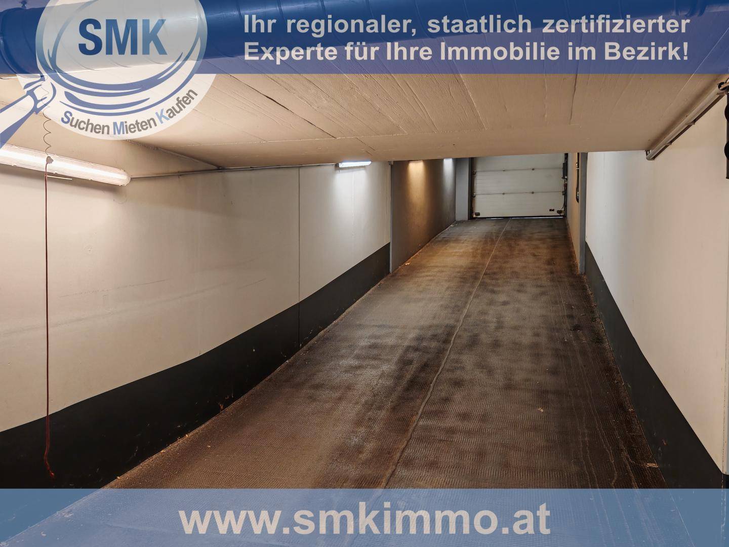Einfahrtsrampe zu einer Tiefgarage mit Betonwänden und Beleuchtung an der Decke.