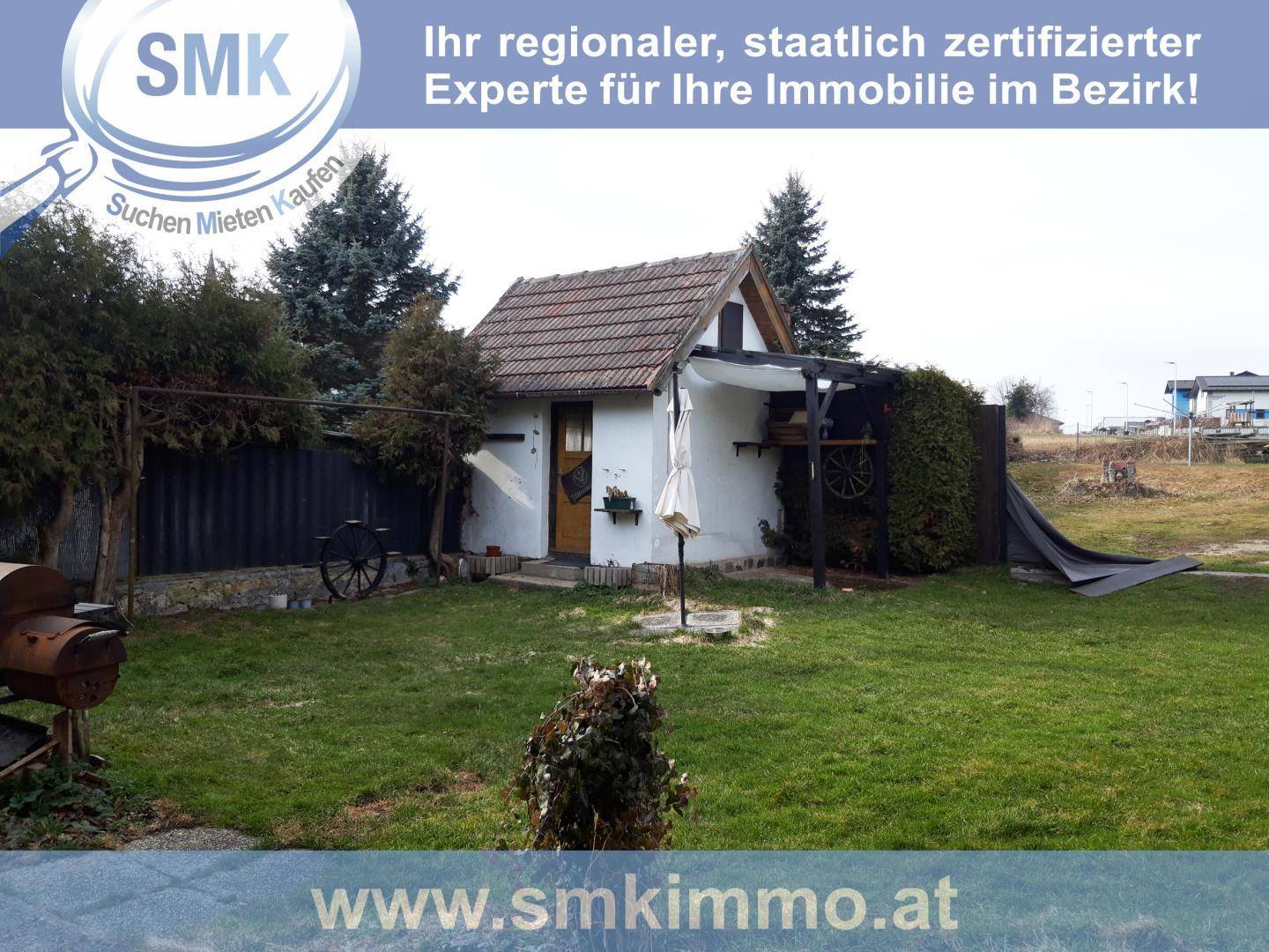 Kleines rustikales Gartenhaus mit Rasenfläche und Bäumen im Hintergrund.