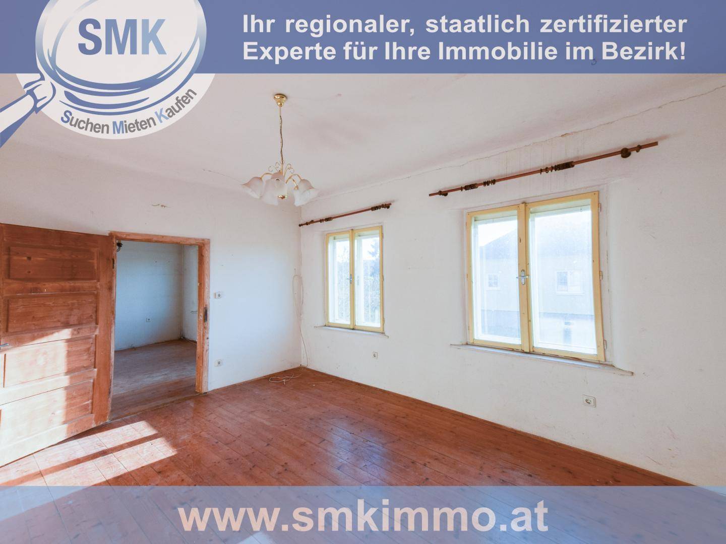 Leeres Zimmer mit Holzdielenboden, weißen Wänden und zwei großen Fenstern, die viel Licht hereinlassen.