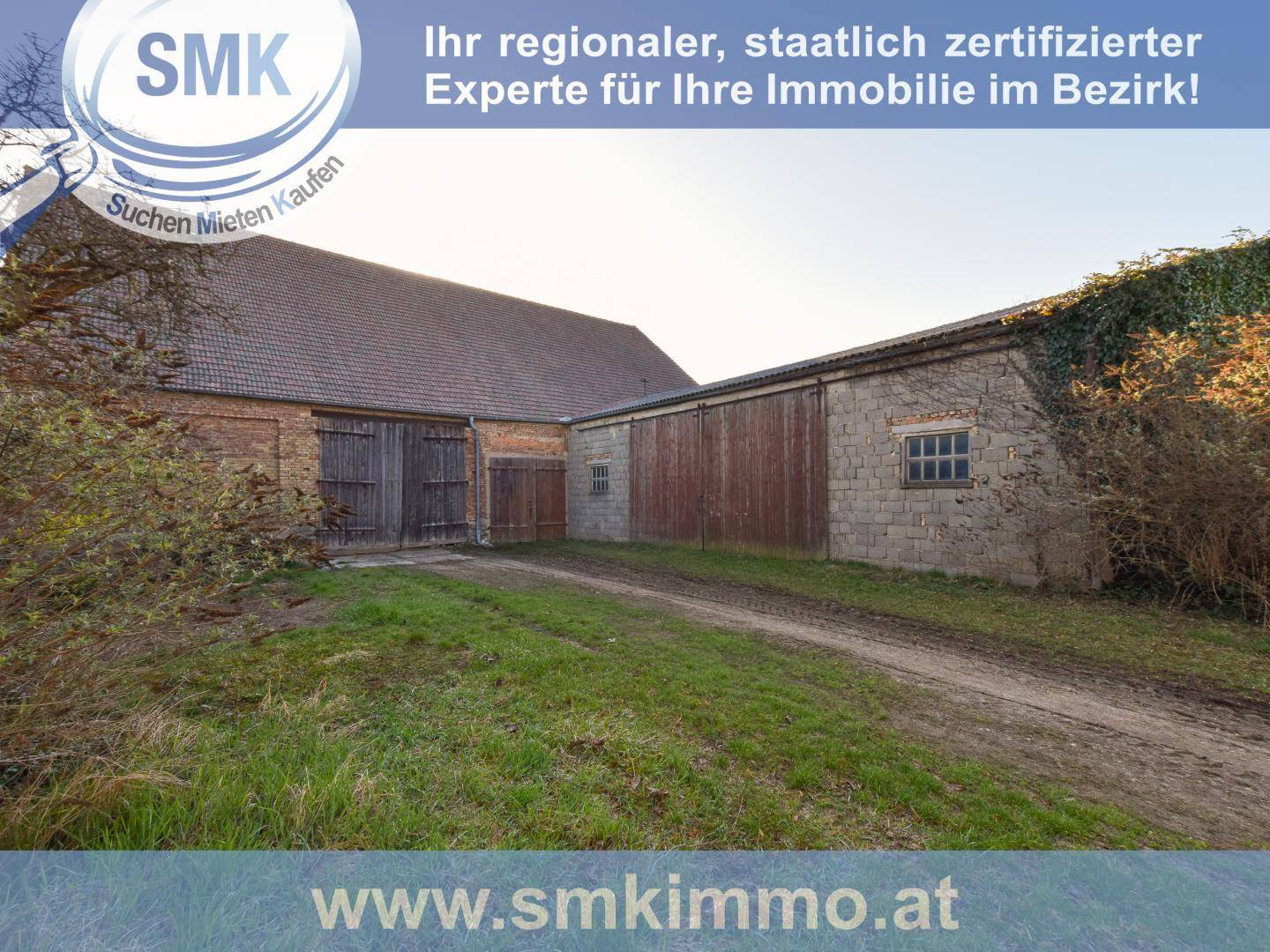 Alte landwirtschaftliche Gebäude mit Holztoren und Steinmauern, umgeben von Gras und Büschen.