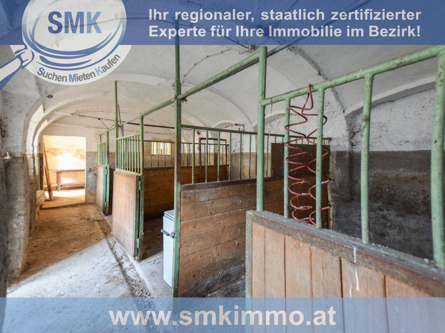 Alte Stallungen mit Holztrennwänden und Metallgittern, die auf eine frühere Nutzung hinweisen.