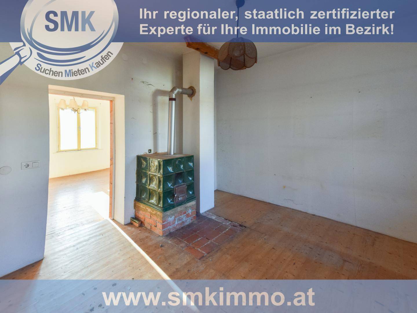 Geräumiges Zimmer mit traditionellem Kachelofen, Holzdielenboden und Blick in einen weiteren Raum.