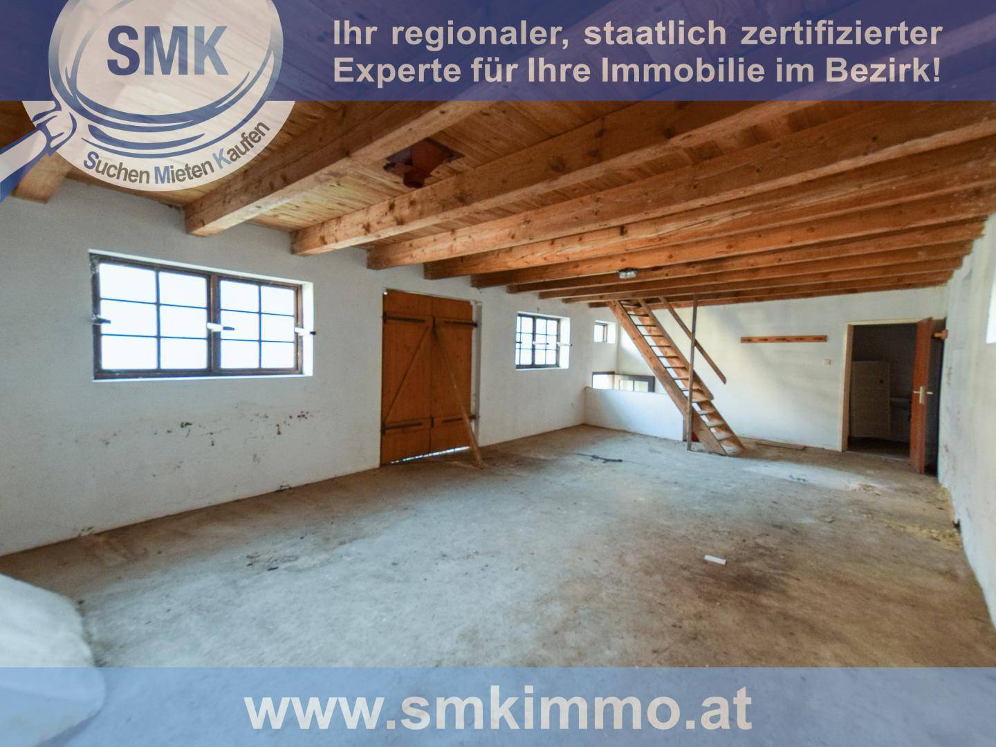 Großer, leerer Raum mit sichtbaren Holzdeckenbalken, Betonboden und einer Holztreppe.