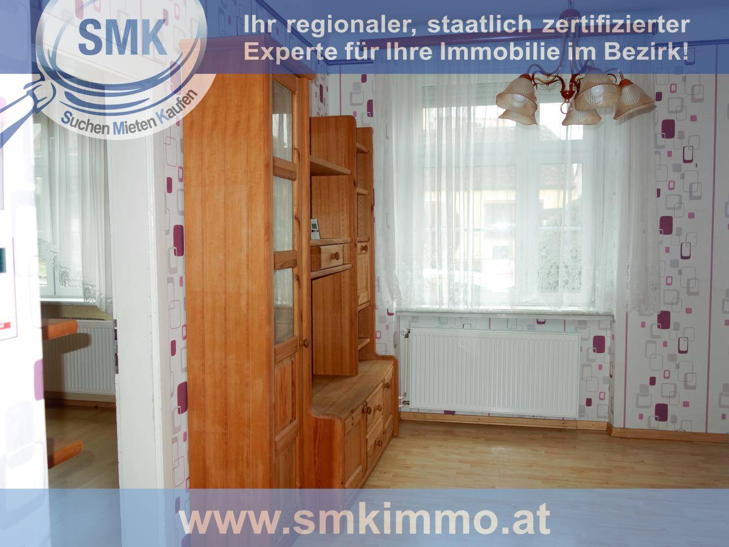 Wohnzimmer mit gemusterter Tapete, Holzschrank und großem Fenster mit Vorhängen.