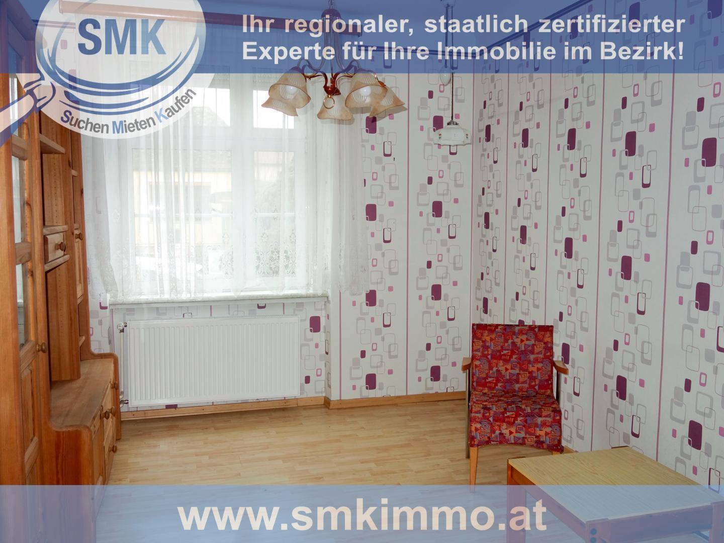 Gemütliches Wohnzimmer mit gemusterter Tapete, Sessel und Holzboden mit viel Tageslicht.