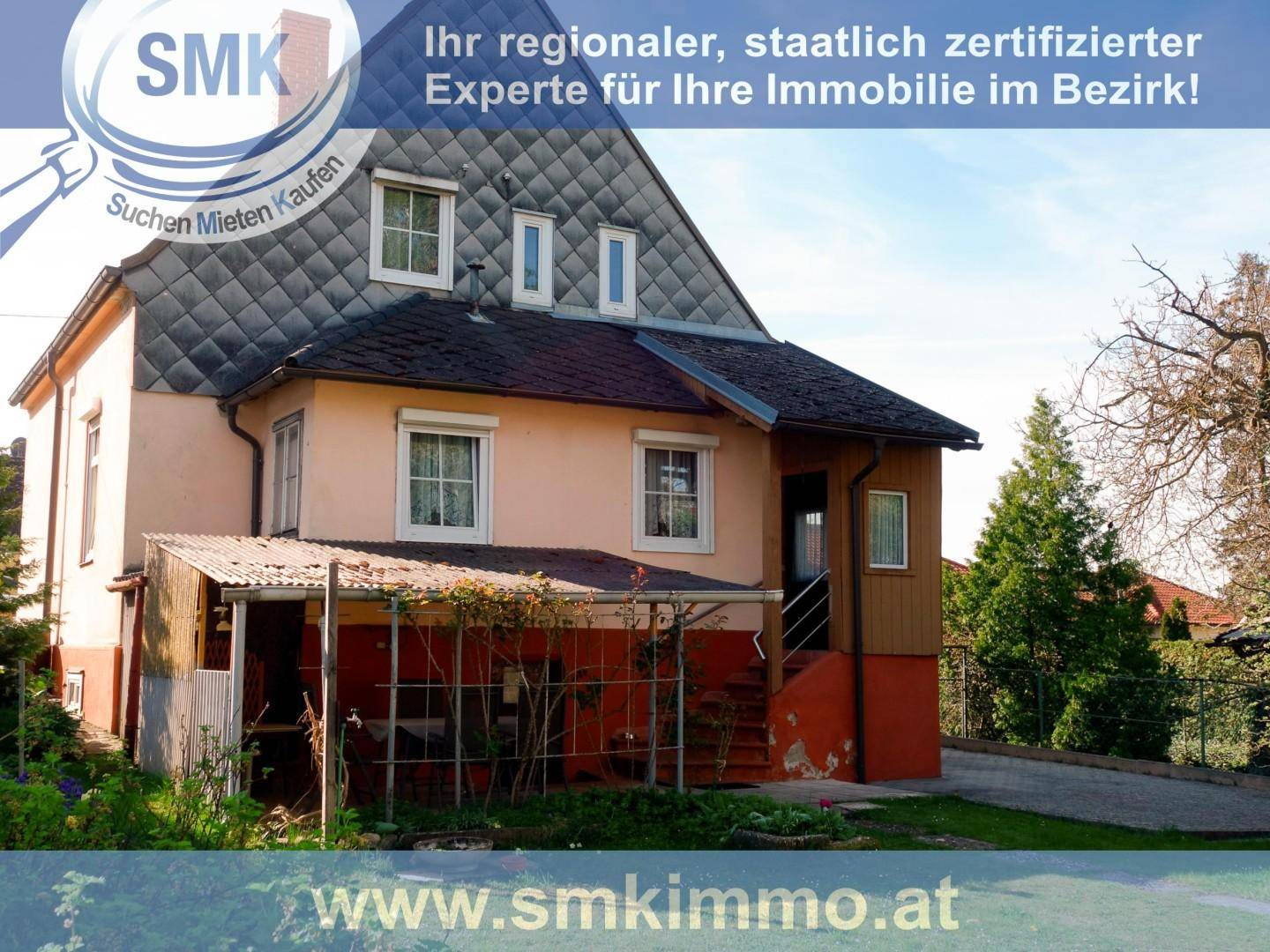 Rückseite des Hauses mit überdachtem Bereich und Treppe im Freien, umgeben von Bäumen.