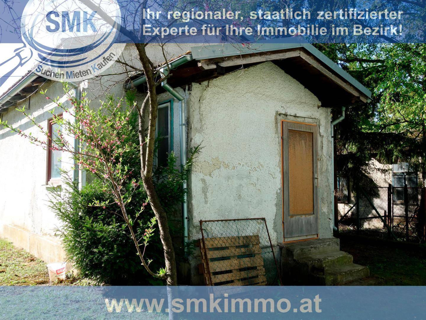 Kleiner Schuppen im Garten mit verputzter Fassade und Holztür, umgeben von Vegetation.