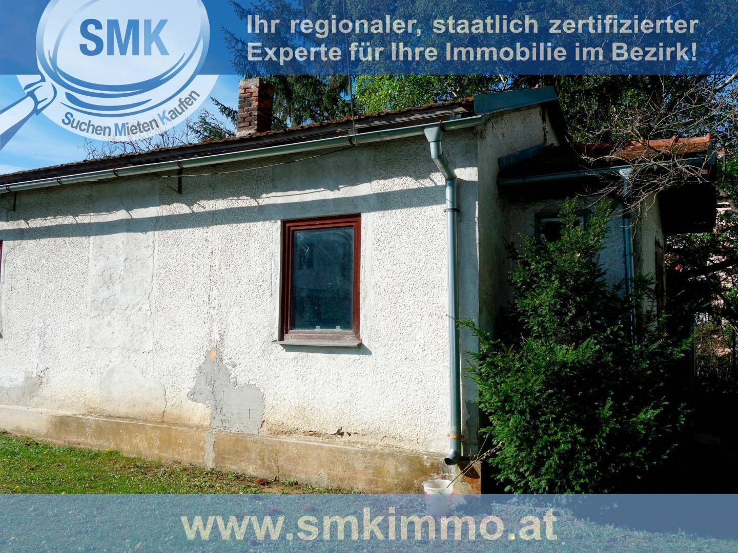 Seitenansicht eines kleinen Schuppens mit verputzter Wand und Fenster im Grünen.