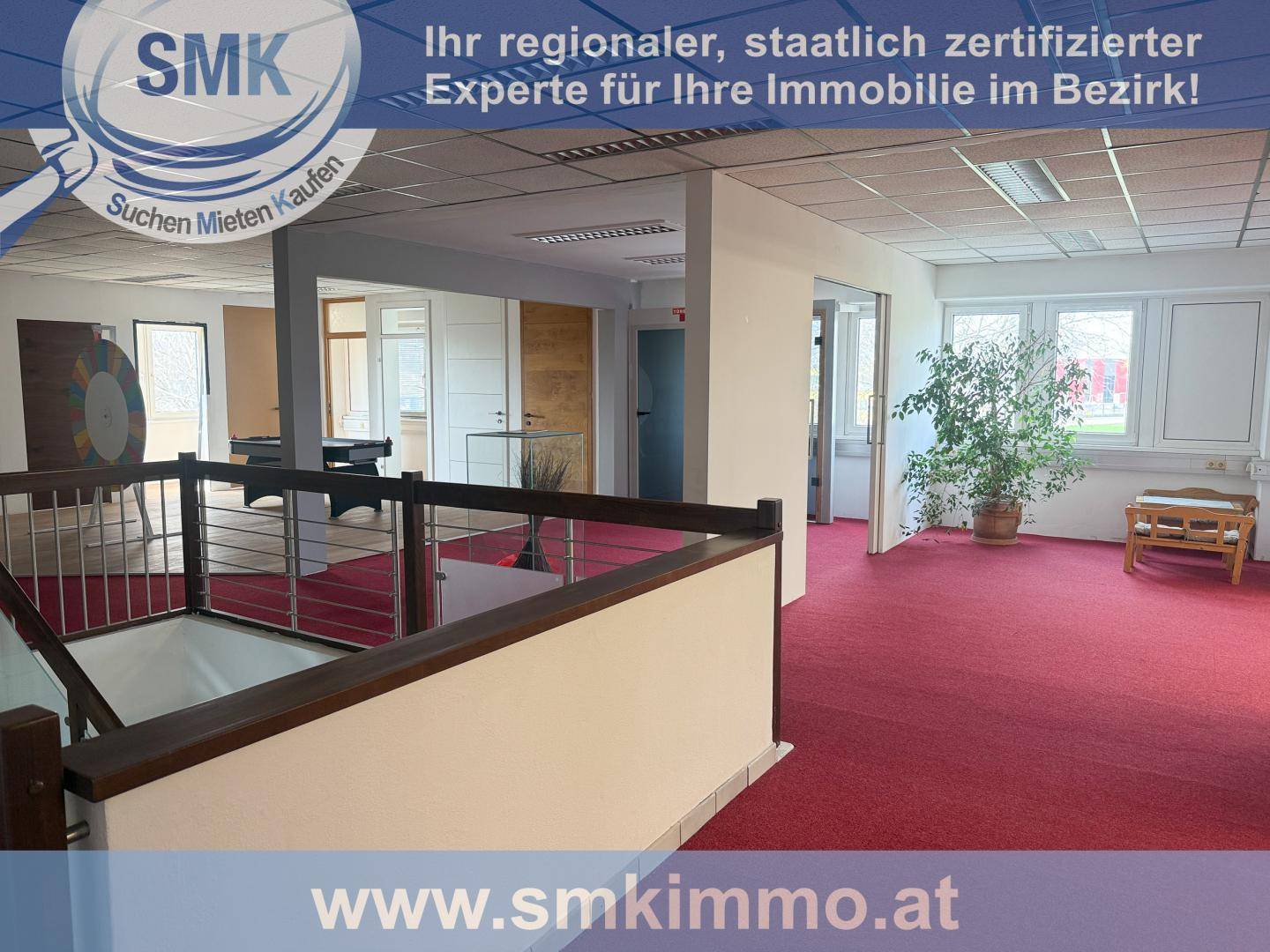 Offener Bürobereich mit rotem Teppichboden, großen Fenstern und Blick auf die untere Etage.