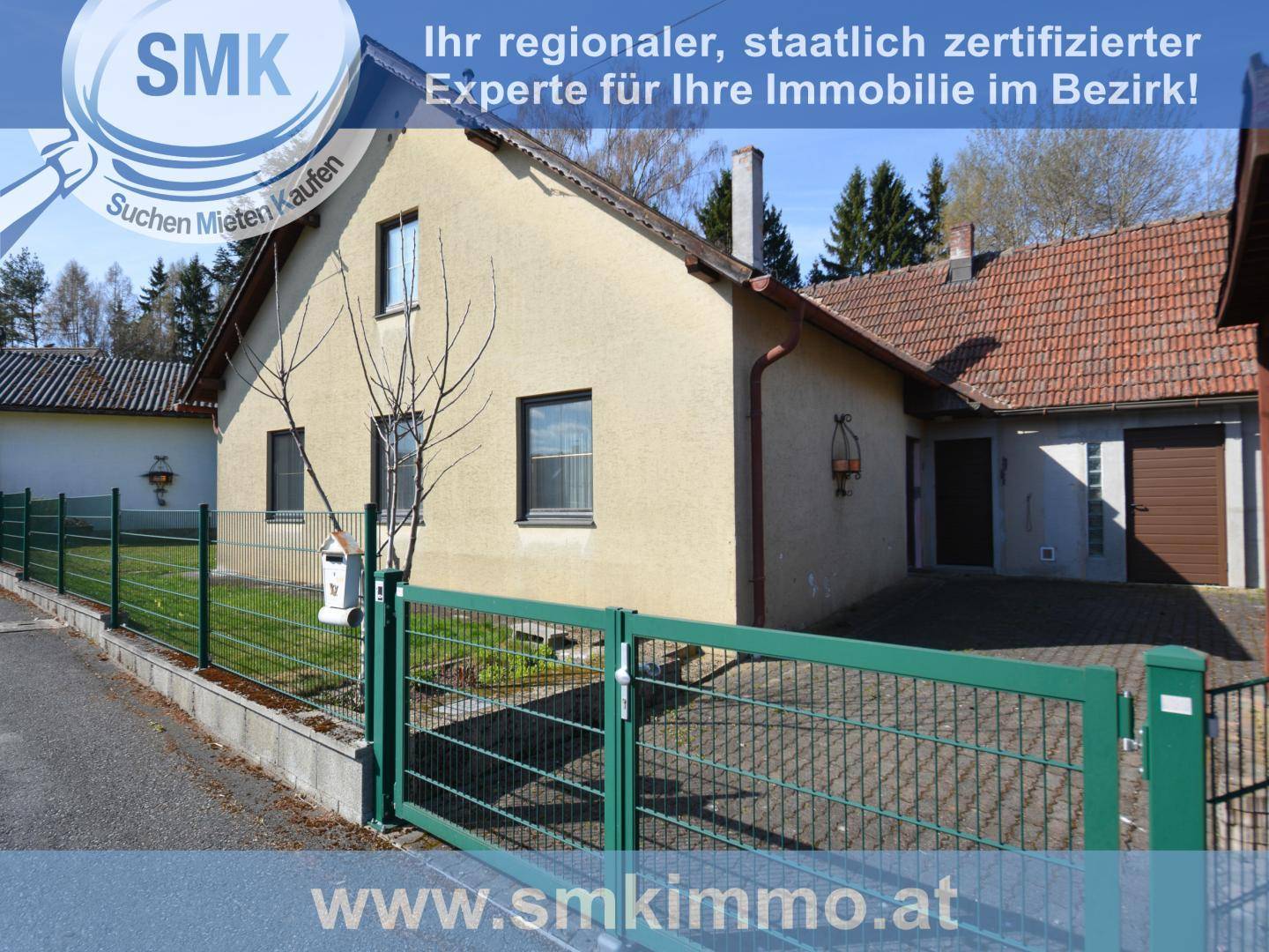Seitenansicht des Hauses mit Zufahrt, grünem Zaun und Einfahrtstor.