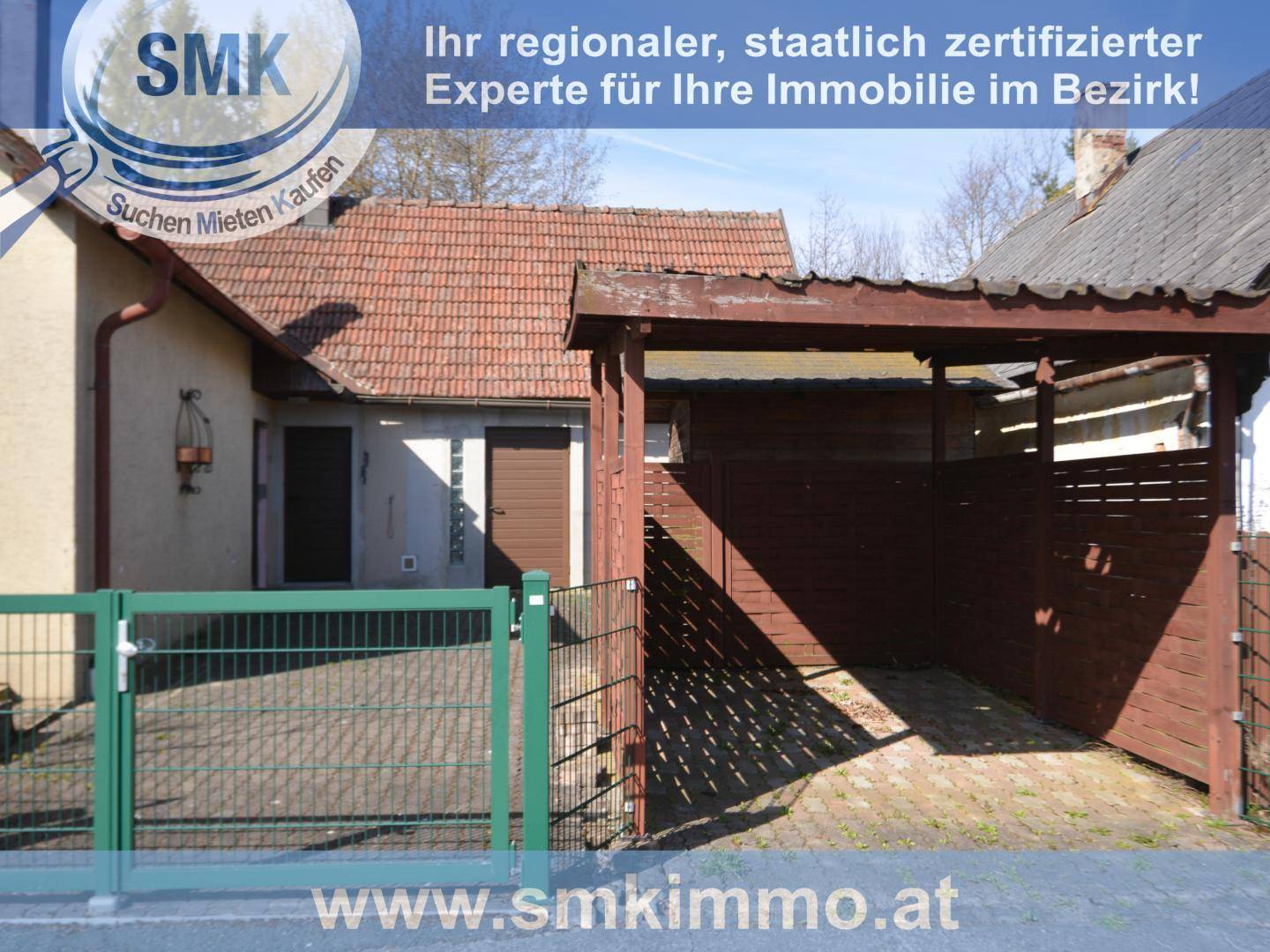 Seitenansicht des Hauses mit Carport, grünem Zaun und Einfahrtstor.