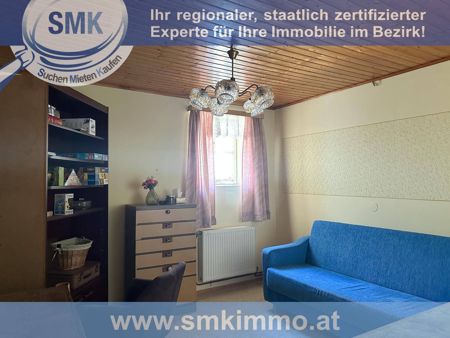 Wohnzimmer mit blauer Couch, Holzdecke und Bücherregal, durch Fenster hell beleuchtet.